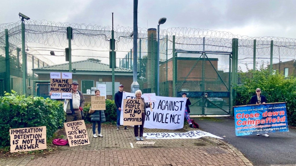 Protesters with placards in front of barbed wire (Photo by Liz Peretz / Geoff Taylor)
