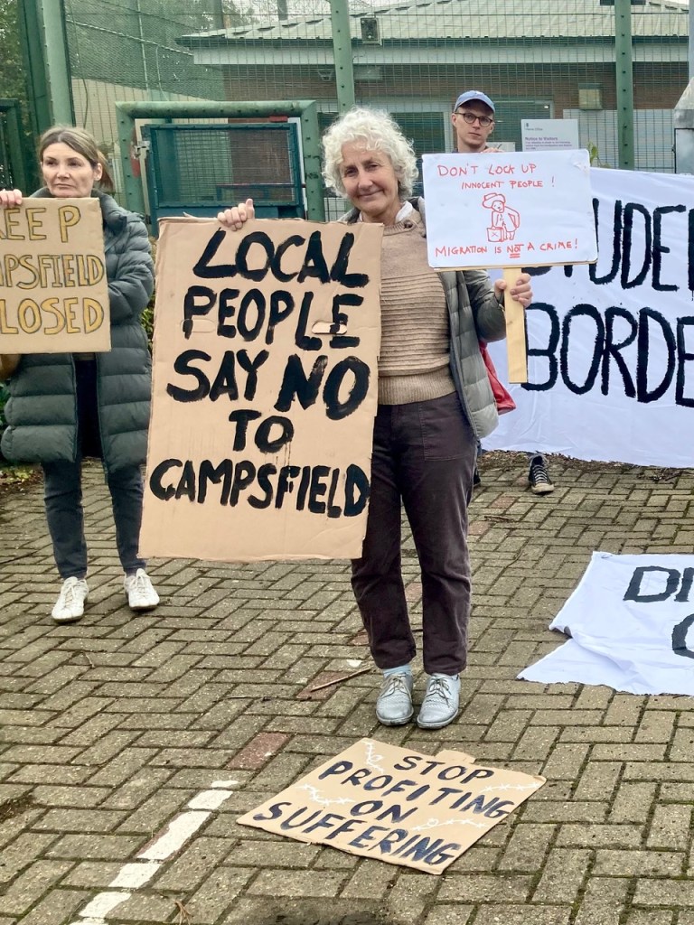 Protesters with placards in front of barbed wire (Photo by Liz Peretz / Geoff Taylor)