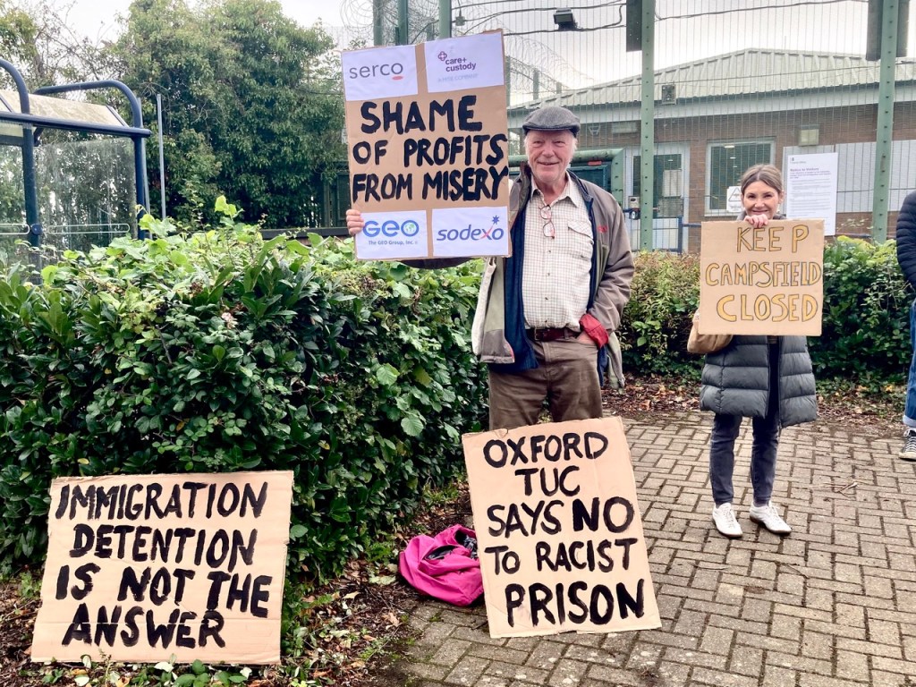 Protesters with placards in front of barbed wire (Photo by Liz Peretz / Geoff Taylor)