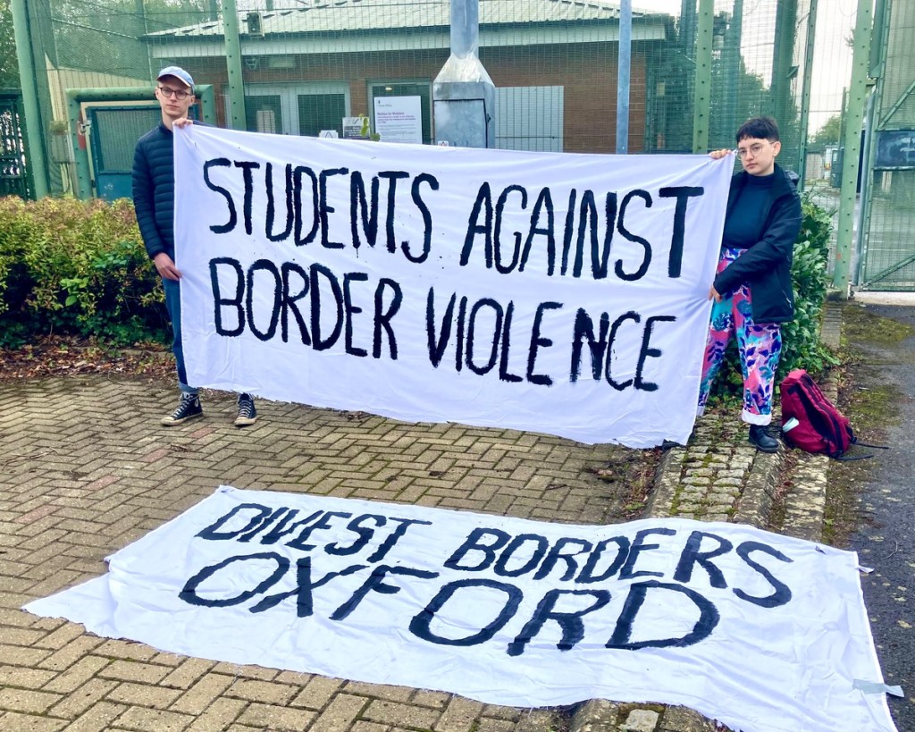 Protesters with placards in front of barbed wire (Photo by Liz Peretz / Geoff Taylor)