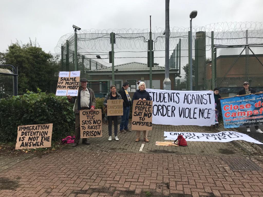Protesters with placards in front of barbed wire (Photo by Liz Peretz / Geoff Taylor)