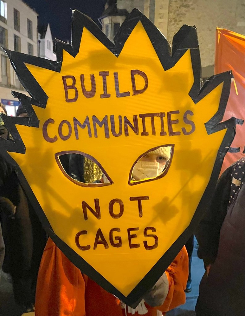 Coalition supporter holds up placard reading "Build communities, not cages"
