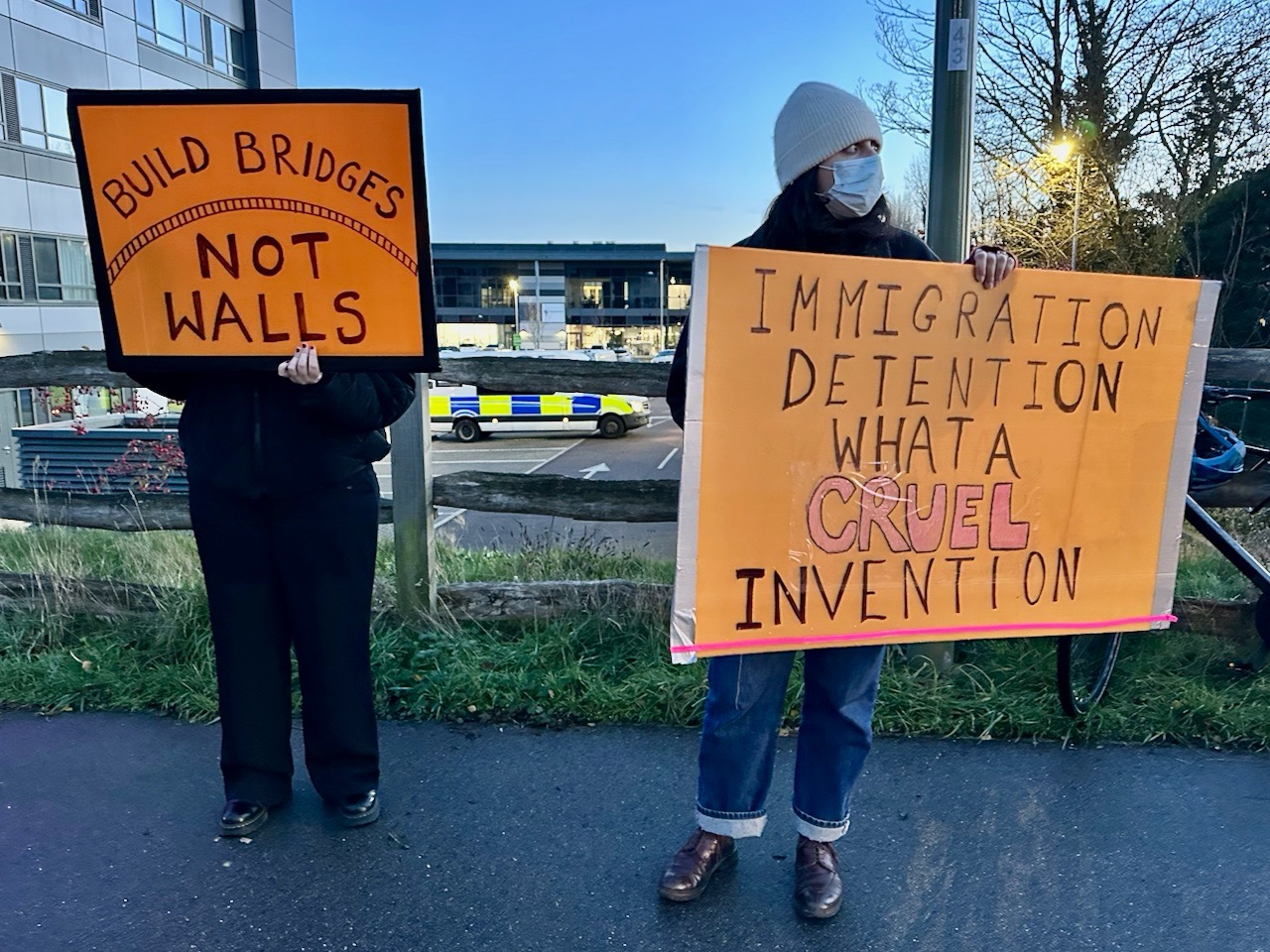 Placards reading "Build bridges not walls" and "Immigration detention. What a cruel invention."
