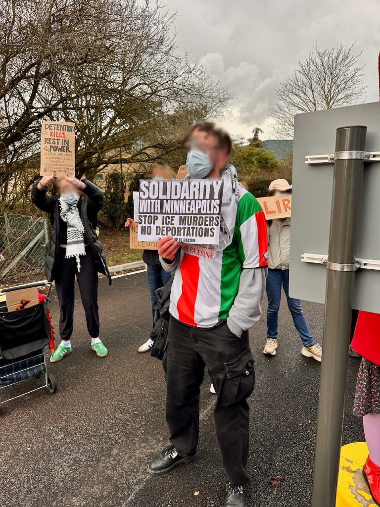 Protestor with a Stand Up To Racism sign reading "Solidarity with Minneapolis. Stop ICE murders. No deportations"