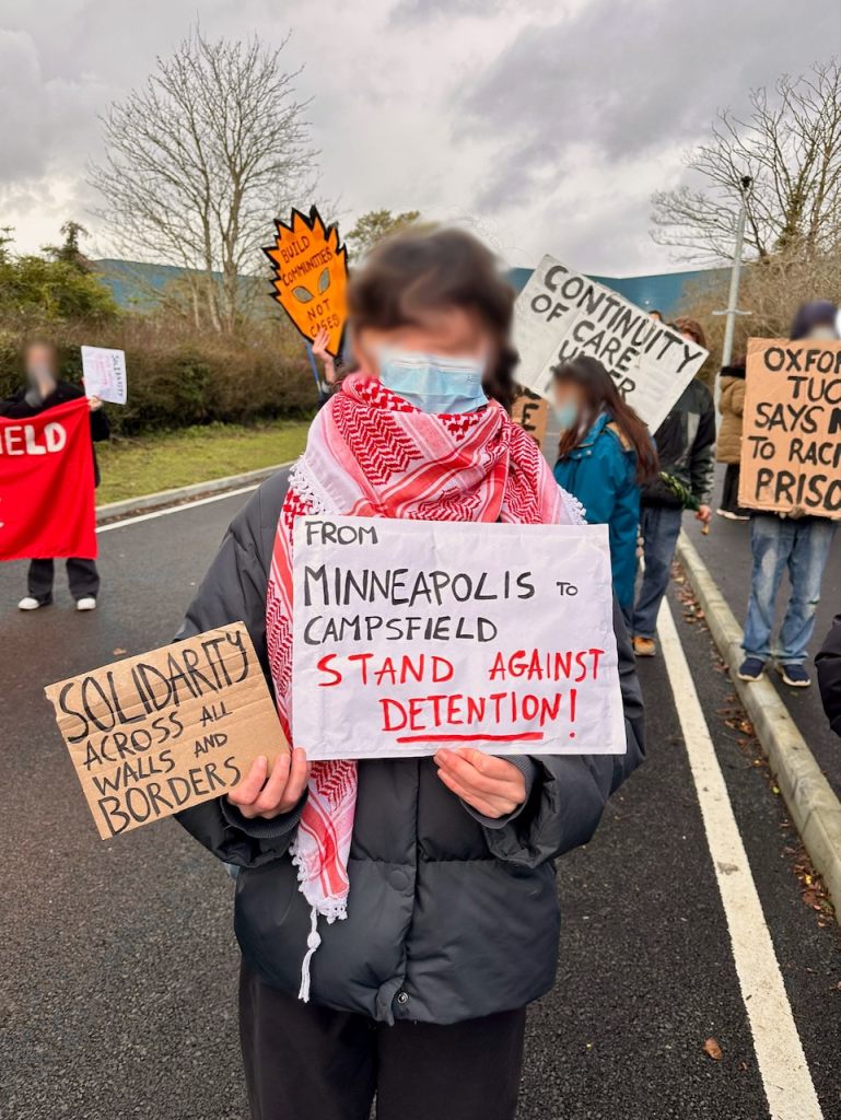Protestor with sign reading "Solidarity across all walls and borders" and "From Minneapolis to Campsfield stand against detention"