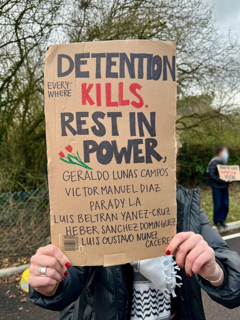Protestor with sign reading "Everywhere detention kills. Rest in power, Geraldo Lunas Campos, VICTOR MANUEL DIAZ, PARADY LA
LUIS BELTRAN YANEZ-CRUZ,
HEBER SANCHEZ DOMINGUEZ,
LUIS GUSTAVO NUNEZ CACERE"