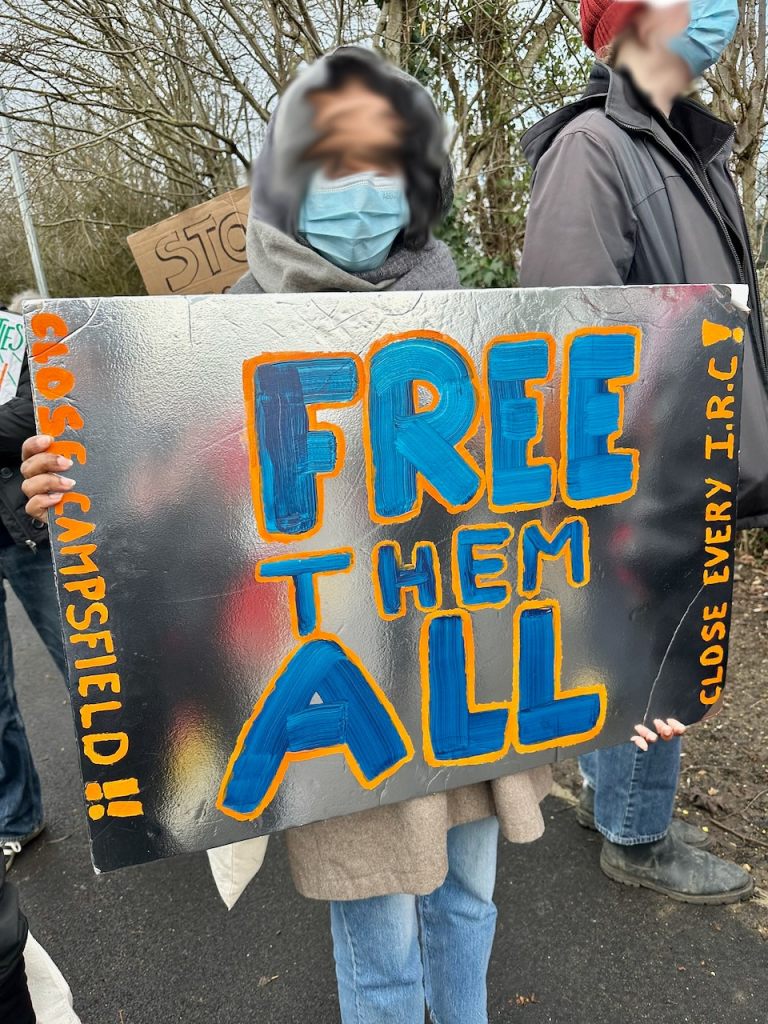 Protestor with sign reading "Free them all. Close Campsfield. Close every IRC"