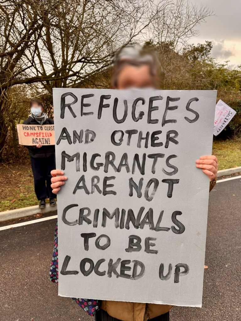 Protestor with sign reading "Refugees and other migrants are not criminals to be locked up"