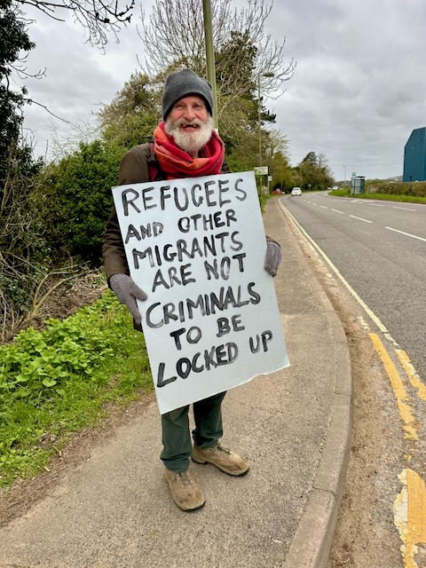29 March, 2026: Close Campsfield campaigner holding placard reading "Refugees and other migrants are not criminals to be locked up" (Photo: Geoff Taylor)