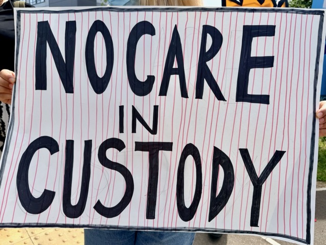 Placard reading "No care in custody"